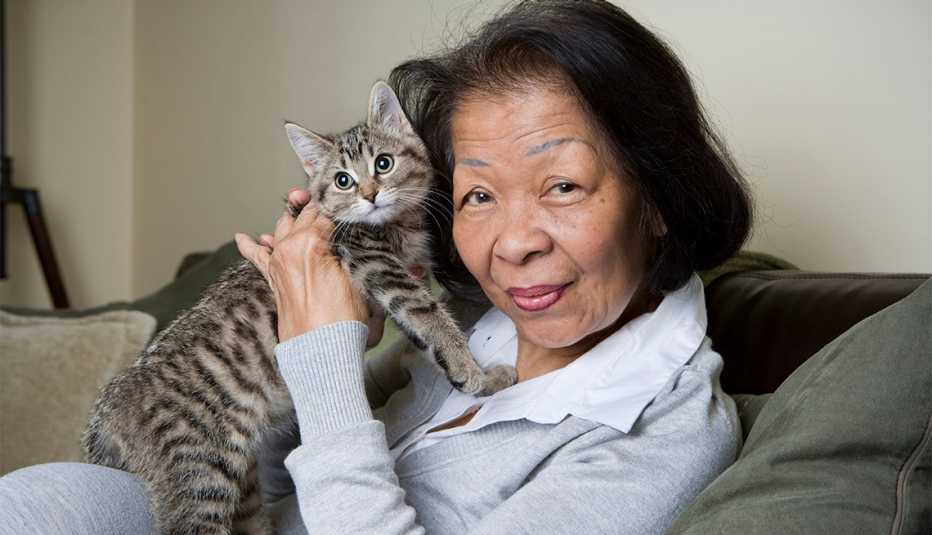 Mujer sostiene a su gato mientras está en el sofá de su casa