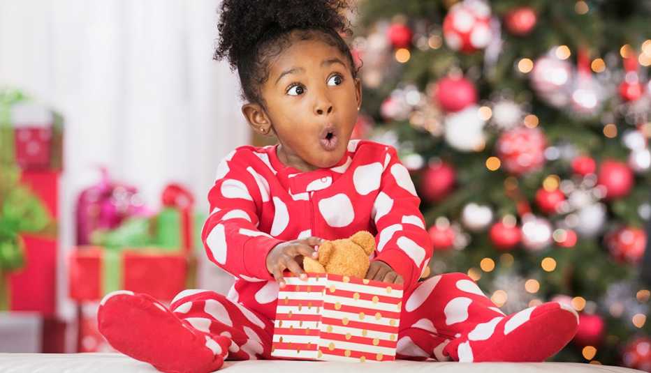 Una niñita con cara de emoción mientras abre un regalo de navidad