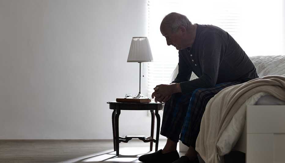 Abuelo sentado en la cama mira al suelo - Huérfanos de la tercera edad 