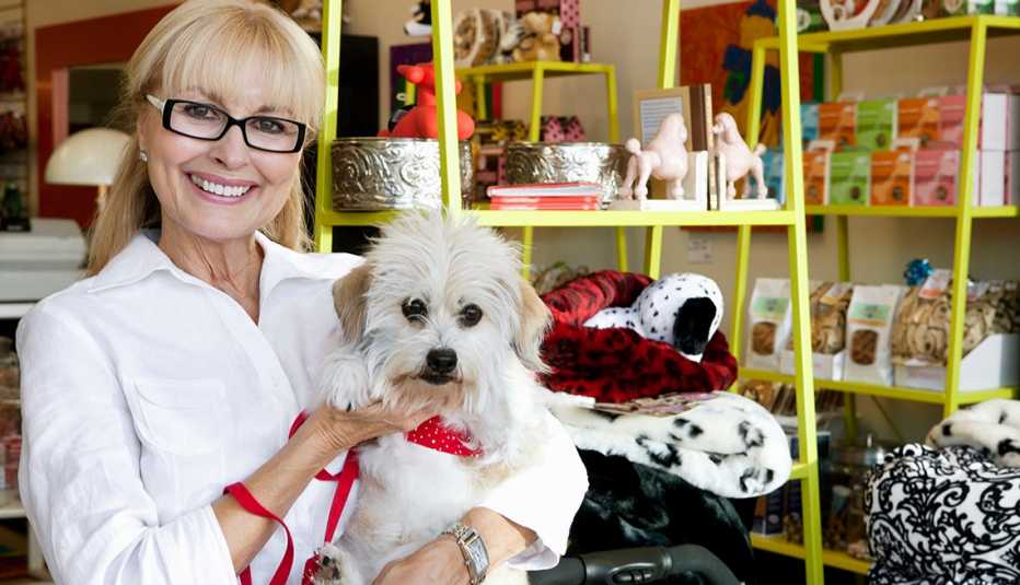 una mujer sonriente sostiene un perro en una tienda de artículos para mascotas que ofrece regalos para el Día Nacional del Perro 