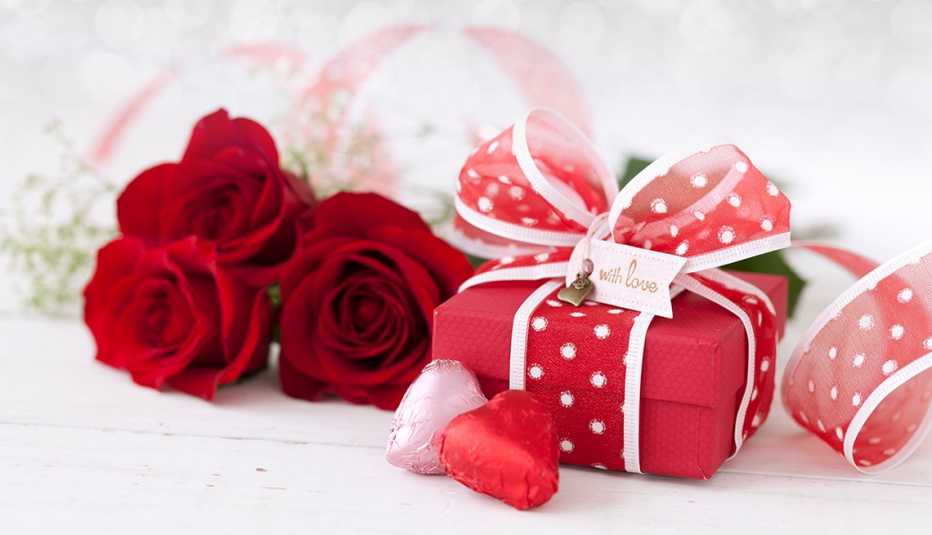 Rosas rojas y una caja de regalo envuelta en un lazo rojo.