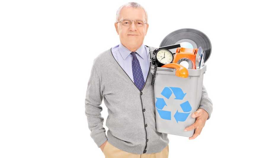 Un hombre mayor sostiene una papelera de reciclaje llena de cosas viejas