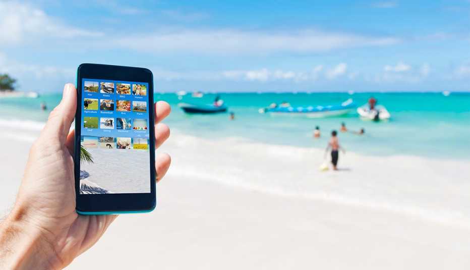 Mano de una persona sostiene un teléfono inteligente y al fondo se ve una playa de Punta Cana, República Dominicana