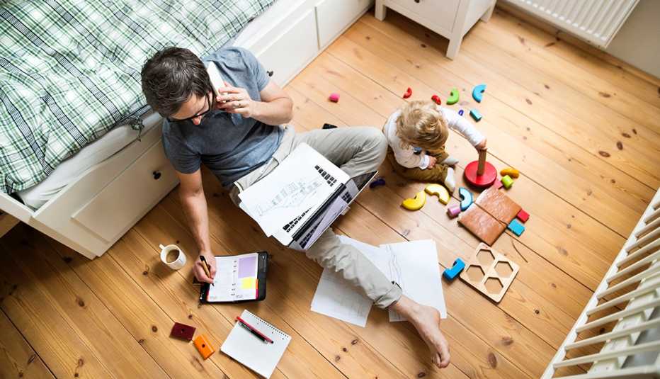 Un hombre trabajando en casa mientras su hijo juega al lado.