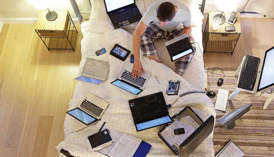 Hombre sentado en la cama rodeado de computadoras