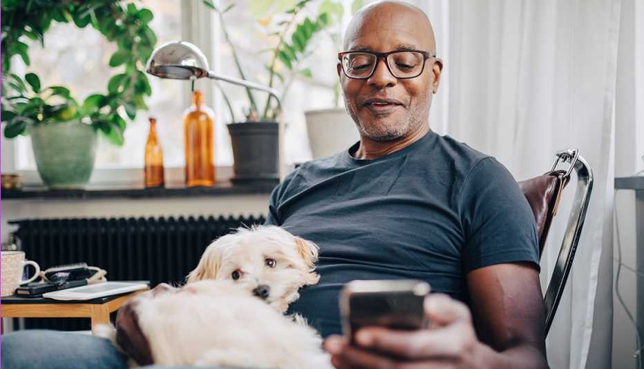 Hombre sonríe mientras mira su teléfono inteligente con su perro en las piernas