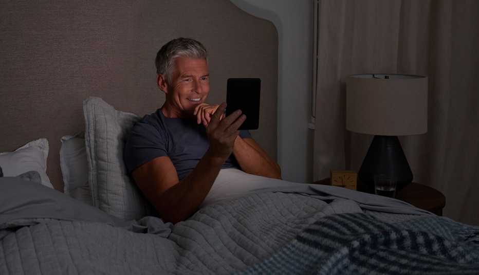 Hombre sonríe mientras lee su lector electrónico en la cama
