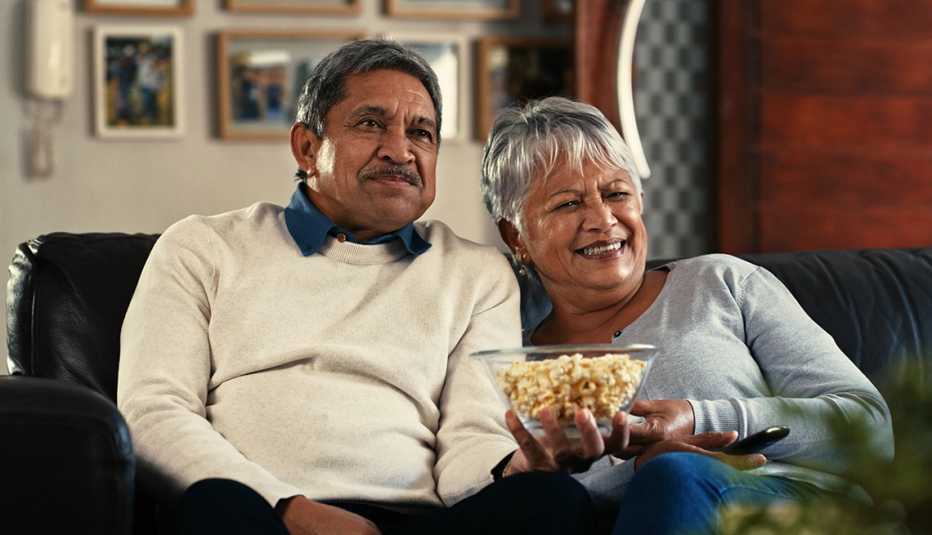 Un hombre y una mujer comen crispetas mientras ven la televisión
