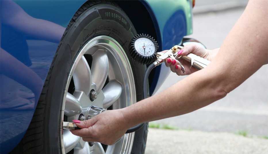 Mujer revisa la presión de aire de los neumáticos de un auto