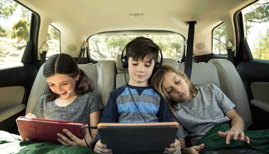 3 niños observan sus tabletas electrónicas mientras van en un auto