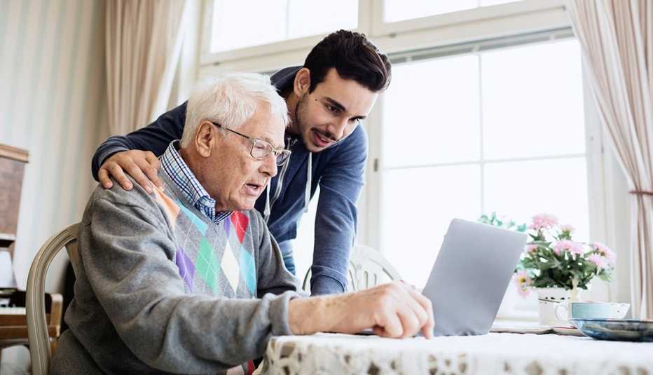 Hombre mayor frente a un computador portátil y hombre joven a su lado