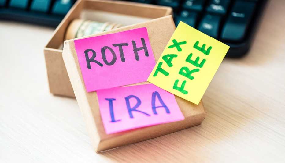 Papeles de notas que dicen ROTH IRA y libre de impuestos al lado de una caja con dólares enrollados.