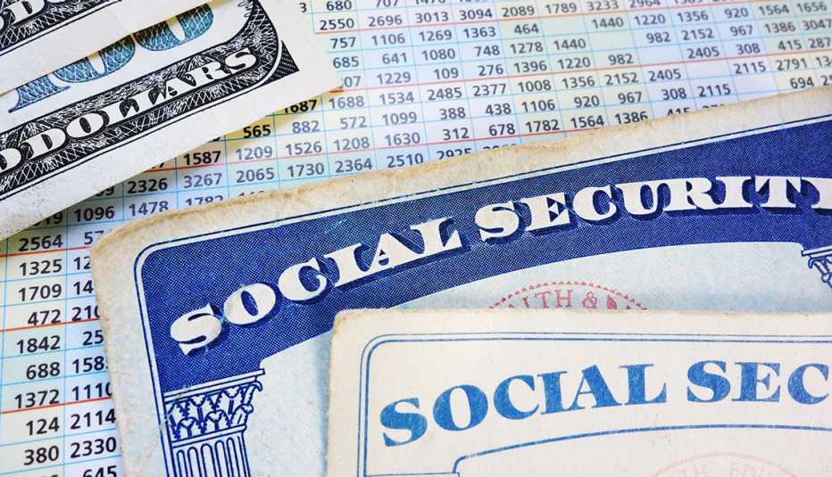 Tarjeta nueva y vieja del Seguro Social sobre un listado de cifras por año y billetes de 100 dólares