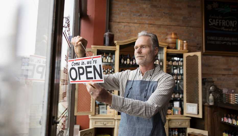 Hombre en una tienda de especias sostiene un letrero en inglés de 'Entre, está abierto'.
