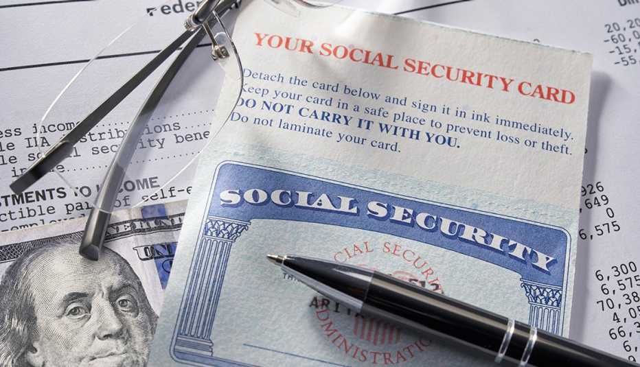 Tarjeta del Seguro Social sobre un billete de 100 dolares, unos lentes, un lapicero y un documento.