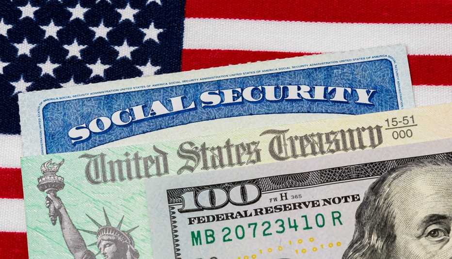Billete de 100 dólares encima de un bono del tesoro, una tarjeta del Seguro Social y la bandera de Estados Unidos