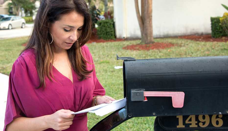 Mujer viendo un estado de cuenta de su salario que retira del buzón del correo de su casa