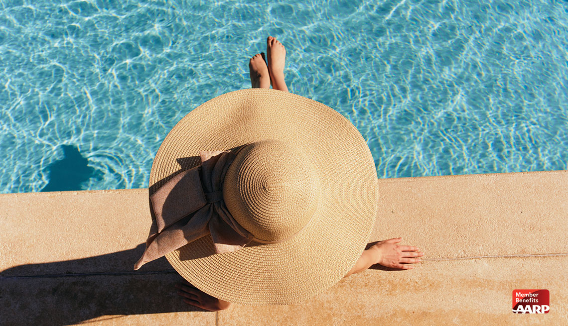  Una mujer con un sombrero de playa sentada frente a una piscina.