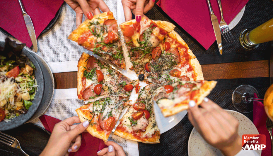 Varias manos sobre una mesa sacando porciones de pizza.