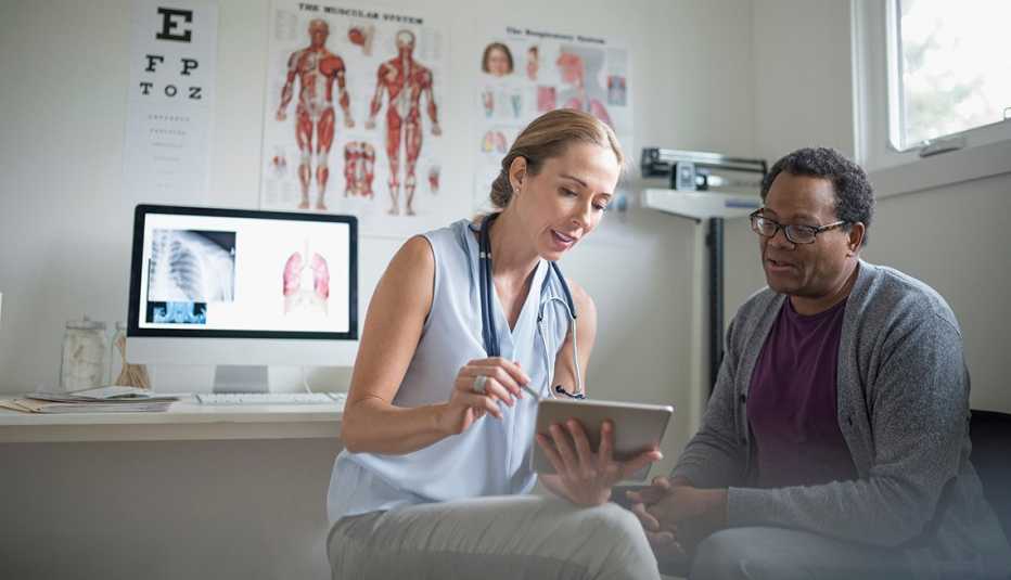 Doctora con tableta digital habla con un paciente masculino mayor en su consultorio.