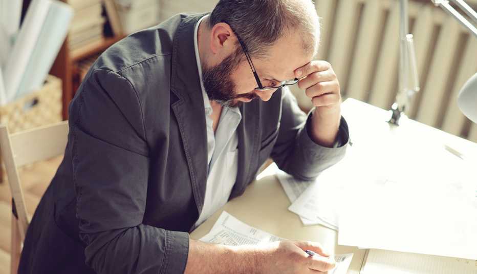 Un hombre observa unos documentos mientras está sentado frente a su escritorio