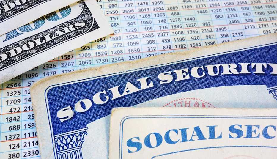 Tarjetas del Seguro Social entre listas de números y billetes de 100 dólares