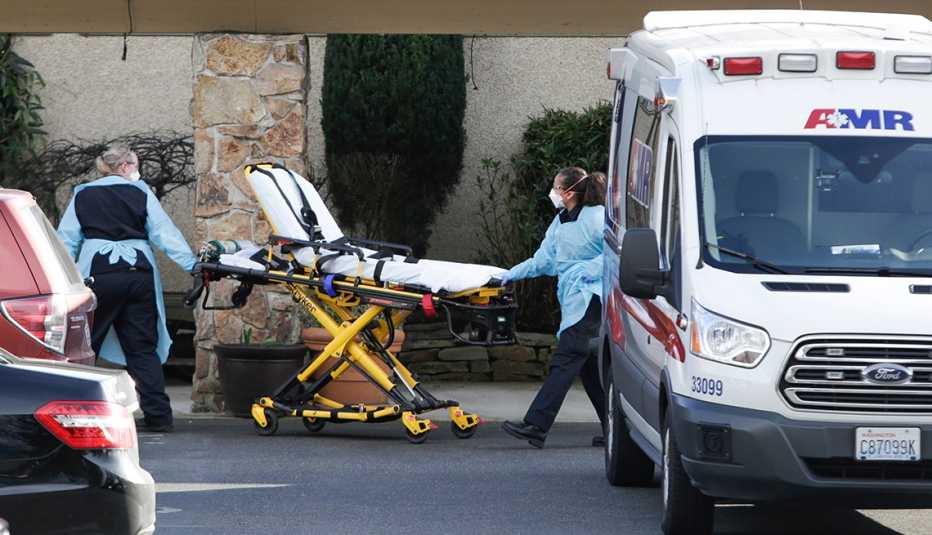 Dos funcionarios de salud empujan una camilla junto a una ambulancia