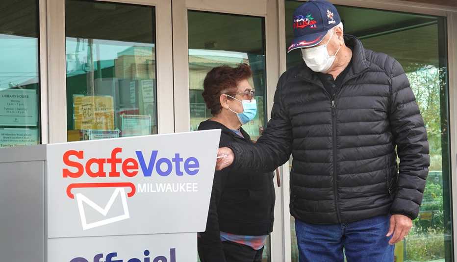 Un hombre, parado junto a una mujer, deposita su voto en un buzón electoral.