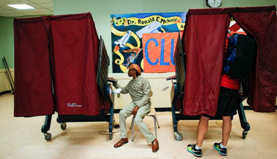 Un hombre vota en una mesa de votación con cortinas rojas en una escuela