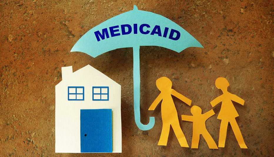 Figuras de papel de una familia frente a su casa, bajo un paraguas de Medicaid