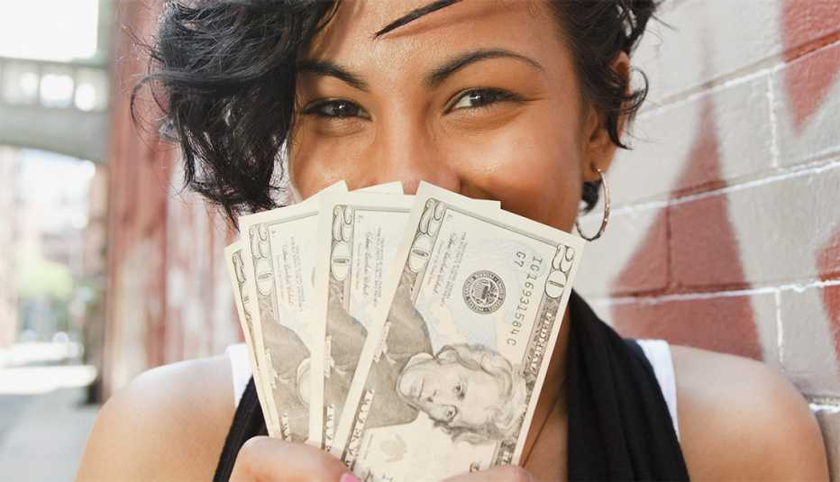 Joven hispana sonriendo y mostrando varios billetes de dolar que sostiene frente a su cara