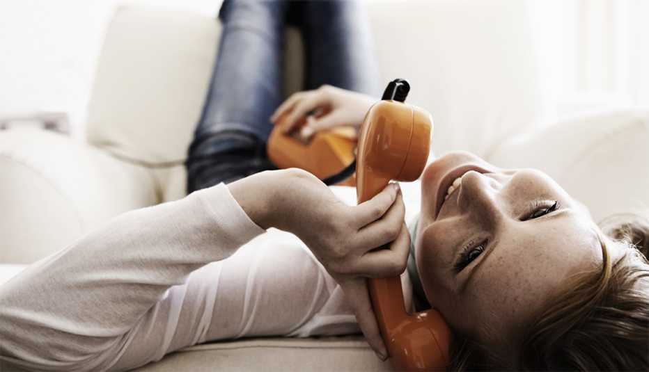 Mujer joven recostada en un sofá hablando por un teléfono fijo