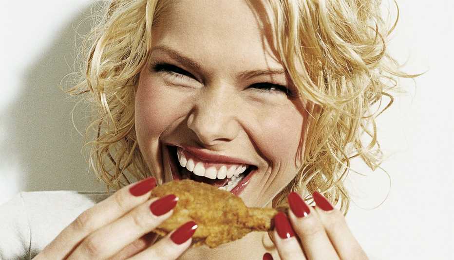 Mujer sonriendo y a punto de comer una pierna de pollo