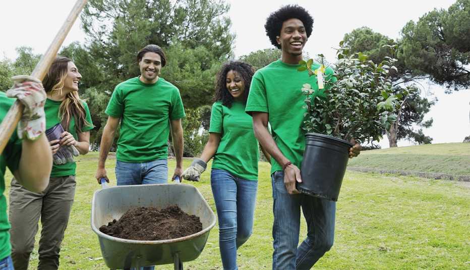 Un grupo de jovenes voluntarios de diferentes razas étnicas con plantas y una carretilla llena de tierra