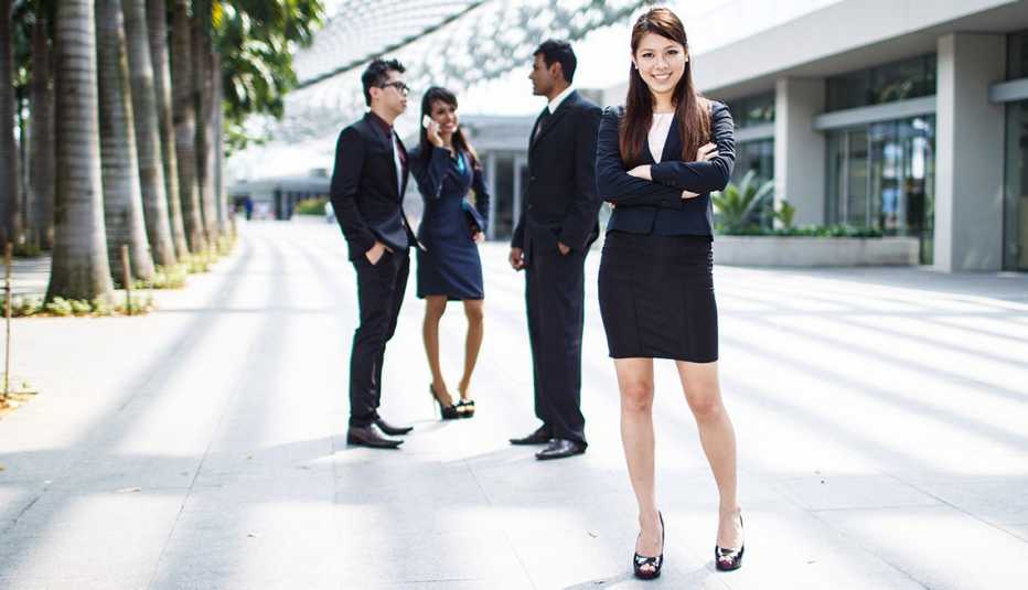 Mujer hispana vestida en traje de oficina, con otras personas detrás con trajes de negocios