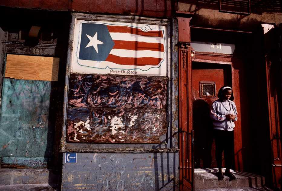 Niña en un portal y al lado un cartel con la bandera de Puerto Rico