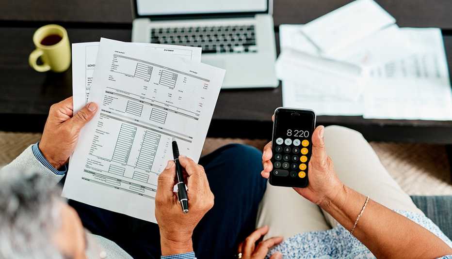 Una vista superior de una pareja haciendo sus impuestos. Una persona tiene el papeleo y la otra una calculadora.