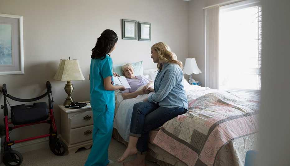 Aumenta la popularidad del cuidado paliativo en el hogar - Dos mujeres hablan con una mujer mayor acostada en una cama
