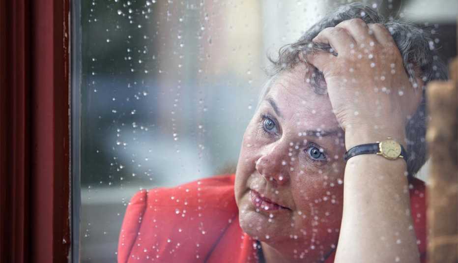 Mujer mayor estresada viendo hacia afuera en la ventana