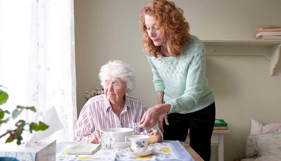 Una mujer alimentando a su madre en una mesa de comedor.