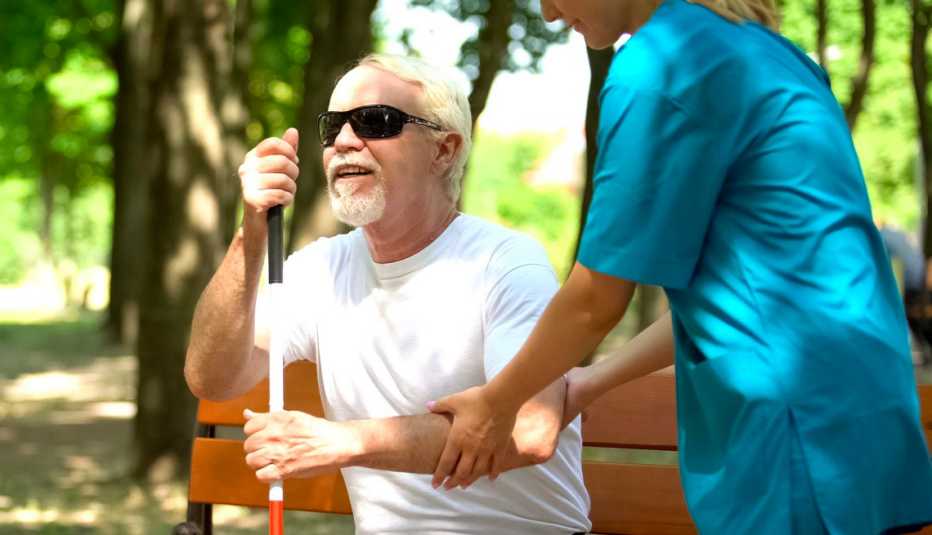 Una enfermera asiste a un adulto mayor ciego en un parque.