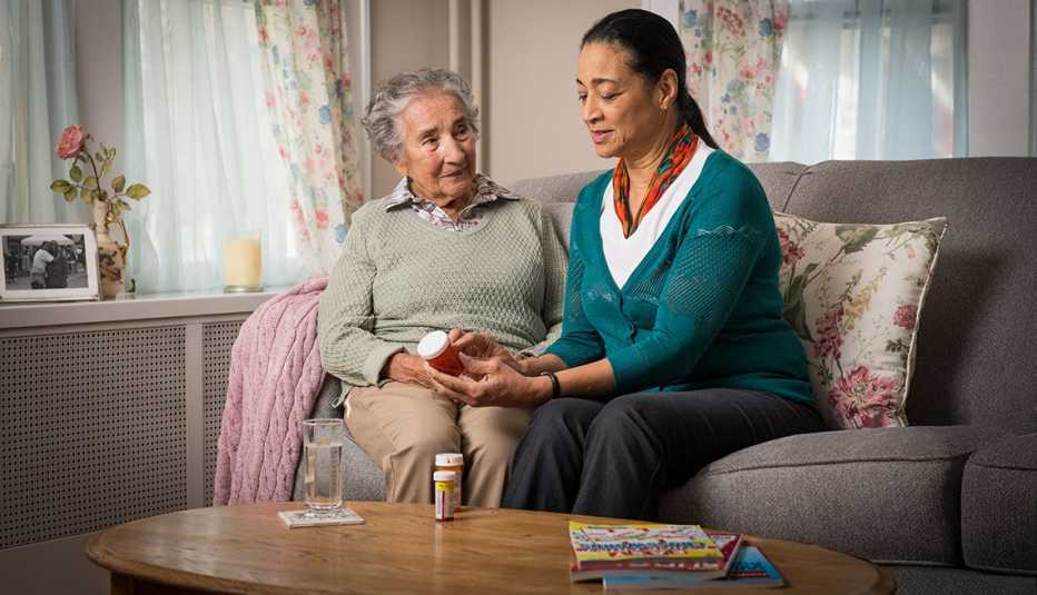 Mujer en edad adulta leyendo un medicamento a una abuelita.