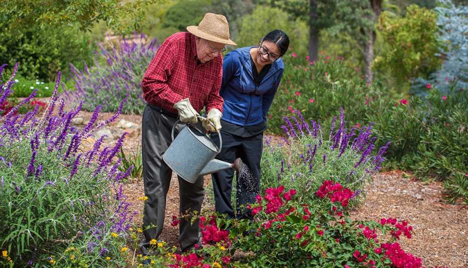 Una mujer acompaña a un hombre mayor mientras riega las plantas