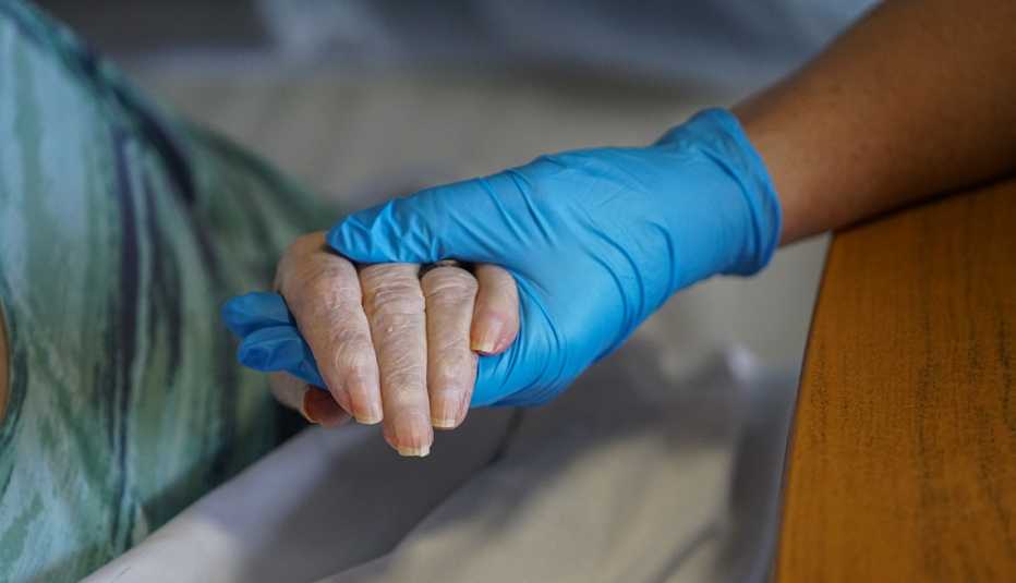 Una enfermera con un guante sostiene la mano del paciente.