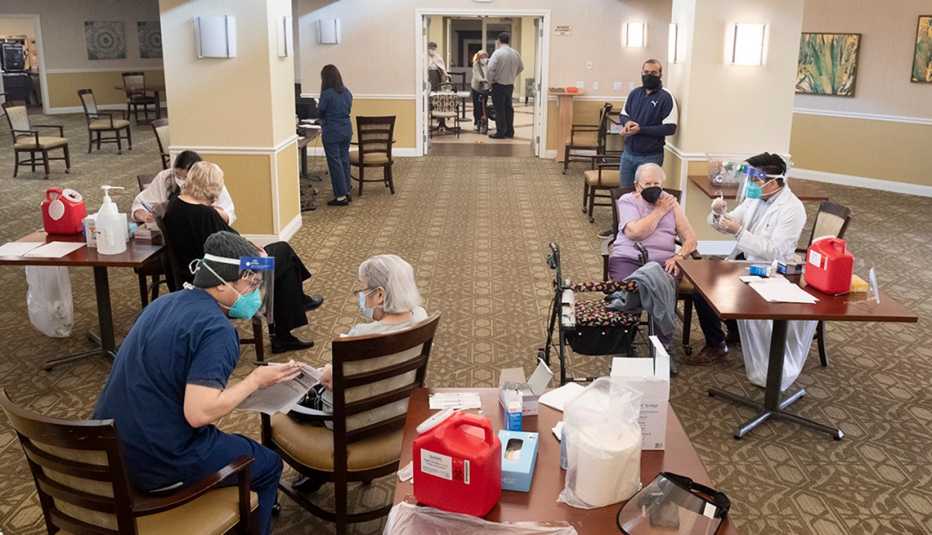 Tres residentes de hogares de ancianos en diferentes mesas recibiendo la vacuna contra la COVID-19.
