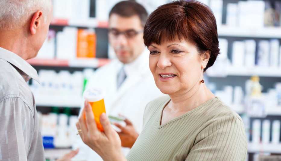 Mujer mayor sostiene un recipiente con medicamentos para el dolor en una farmacia.