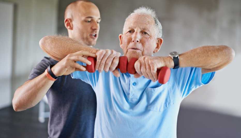 Hombre mayor levanta unas pesas guiado por un entrenador personal.