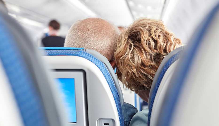 Vista trasera de una pareja madura recostando sus cabezas en un avión.