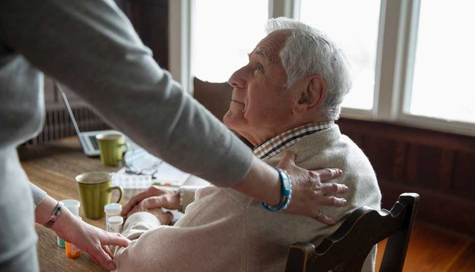 Una persona conforta a un hombre mayor sentado a la mesa