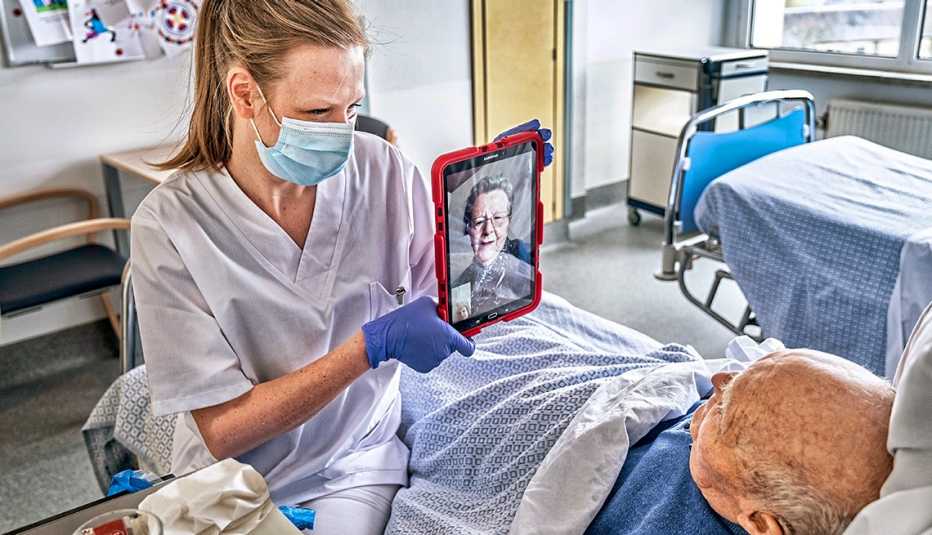 Una enfermera con una mascarilla sostiene una tableta para que un paciente se comunique con su familia